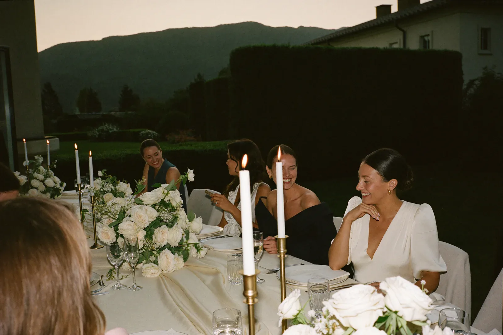 Braut und Freundinnen lachen gemeinsam an einer festlich gedeckten Hochzeitstafel